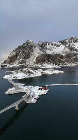 Cinematic aerial view of snowy coastal village and bridge in Lofoten, Norway, scenic arctic seascape with islands, winter shoreline, and dramatic Nordic landscape
