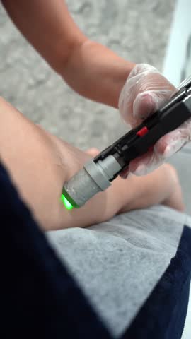 Vertical close up video of professional cosmetologist doing alexandrite laser hair removal of legs to young woman in modern beauty clinic