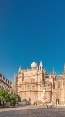 Panorama showing the Seville Cathedral and Giralda Tower timelapse hyperlapse in Seville, Spain. The largest gothic cathedral in the world, located on Virgen de los Reyes square under a blue sky