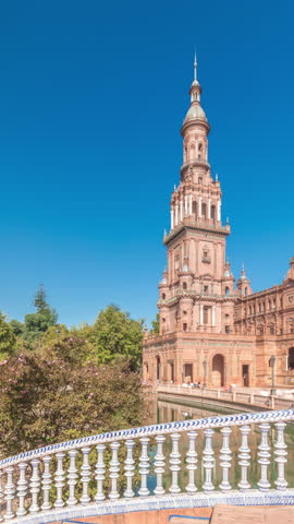 Panorama showing Plaza de Espana in Seville timelapse, a grand architectural complex in Maria Luisa Park built for the Ibero-American Exposition. Bridges, canal and vintage streetlights under blue sky
