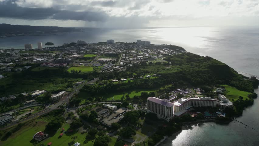 Panoramic aerial overview of coastal village with lush greenery, hotel resort buildings, and residential areas at Tamuning, Guam, USA.