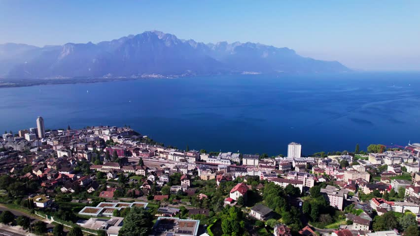 High mountains of French Alps in the background of Montreux cityscape at Lake Geneva in Switzerland seen from above on a sunny hazy day and below the a9 freeway in the foreground