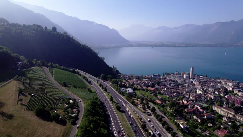 High mountains of French Alps in the background of Montreux cityscape at Lake Geneva in Switzerland seen from above on a sunny hazy day and below the a9 freeway in the foreground