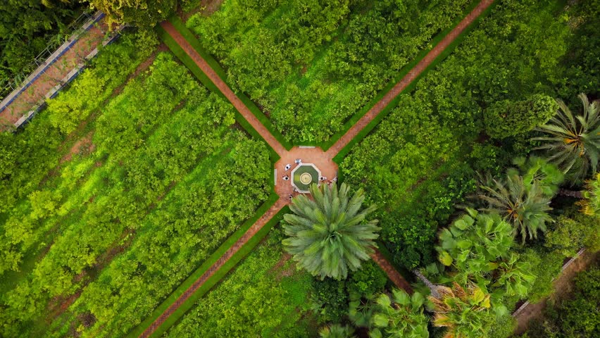 Drone video shows a lush public garden in Spain, with structured greenery, a pool, and architectural elements surrounded by orchards and scenic landscapes.