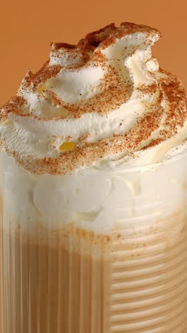 Glass of pumpkin latte with cream and spices close-up on a rotating table.