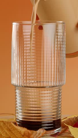 Process of making a pumpkin spice latte. Latte being poured into a glass, close-up footage.