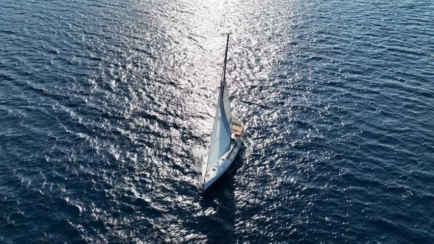 Aerial drone tracking video of beautiful sail boat with white sails cruising deep blue Aegean sea