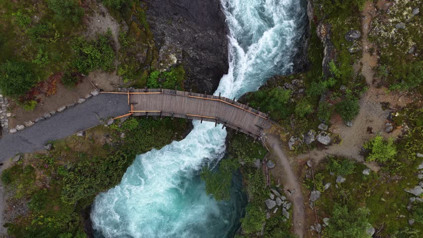 An aerial shot of fast-flowing Tora River and rustic bridge, surrounded by lush green Nordic landscape