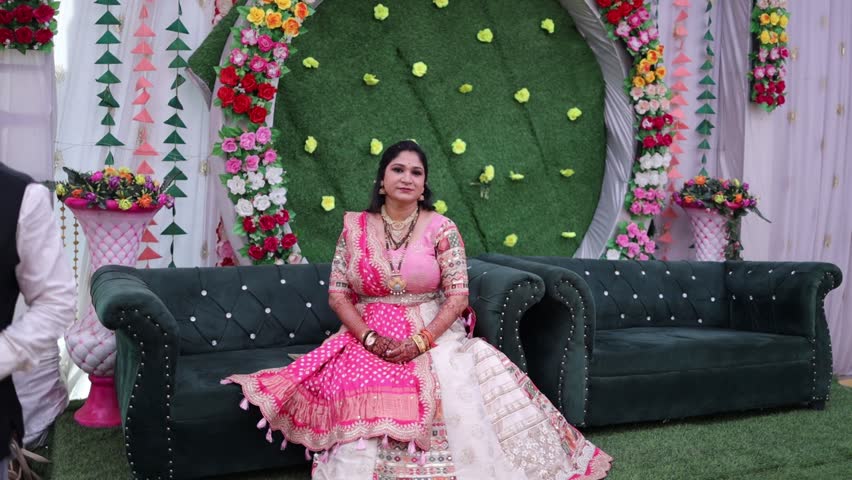 Beautiful Indian woman dressed in an ornate pink lehenga with a contrasting maroon and gold dupatta, posing gracefully at a decorated wedding venue
