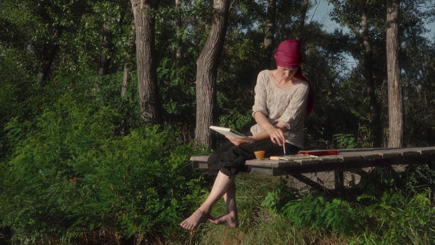 The artist paints a landscape in watercolor while sitting on a wooden pier on the bank of the river