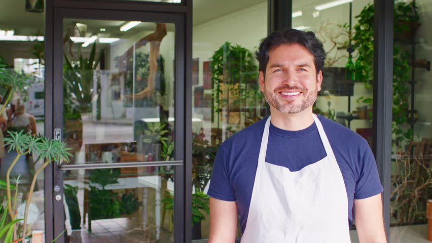 Portrait Of Smiling Male Owner Of Florists Standing In Doorway Surrounded By Plants