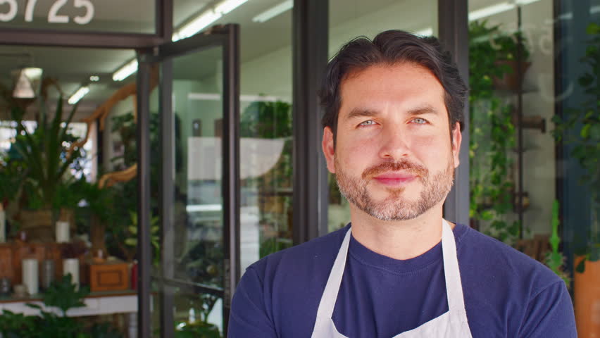 Close Up Portrait Of Smiling Male Owner Of Florists Standing In Doorway Surrounded By Plants