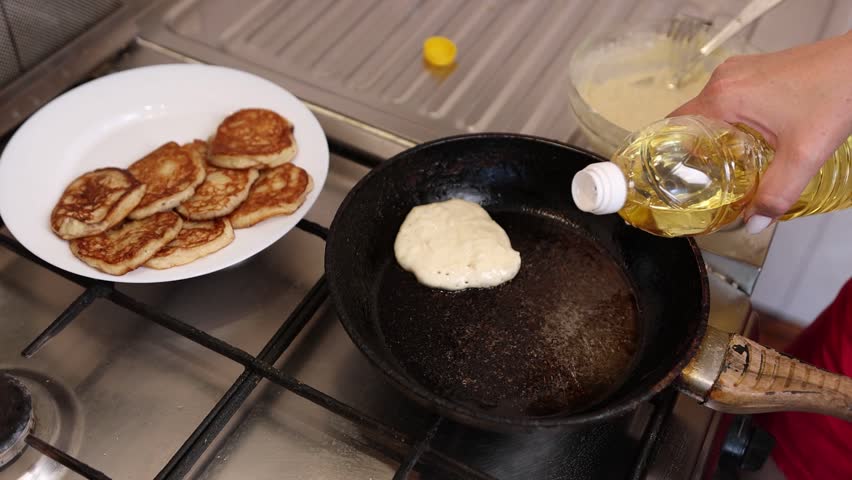 Pouring vegetable oil into a hot frying pan while frying homemade pancakes for breakfast, close-up cooking process.