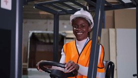Smiling african american female worker driving forklift in warehouse with safety equipment - Powered by Shutterstock - Get 15% off with code: PIKWIZARD15