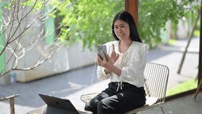 woman is sitting on a chair with a laptop and a cell phone in front of her. She is smiling and holding her cell phone up to her face - Powered by Shutterstock - Get 15% off with code: PIKWIZARD15