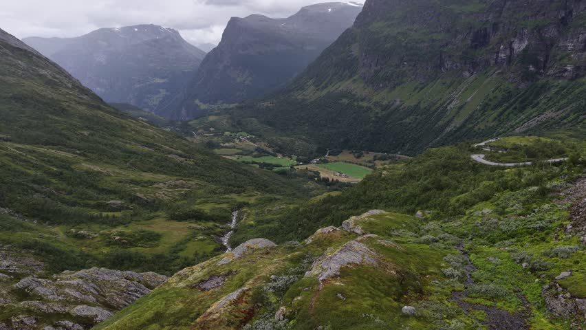An Aerial view of a lush valley with scattered houses, surrounded by steep mountains and forests