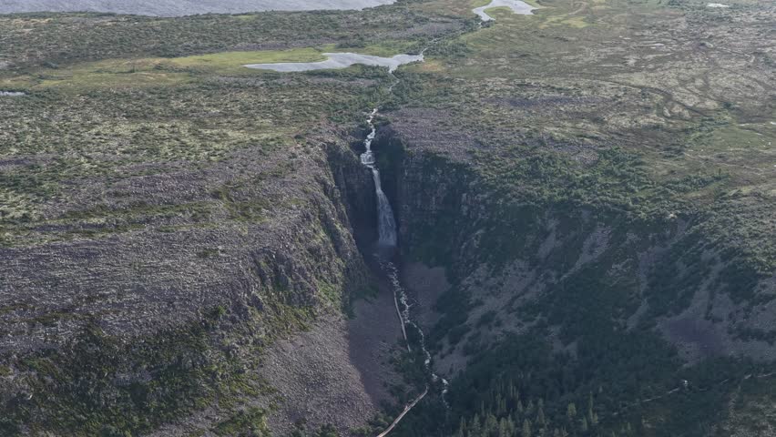A drone view of Njupeskar waterfall plunging down a steep canyon surrounded by untouched tundra and dense forests in Fulufjallet National Park