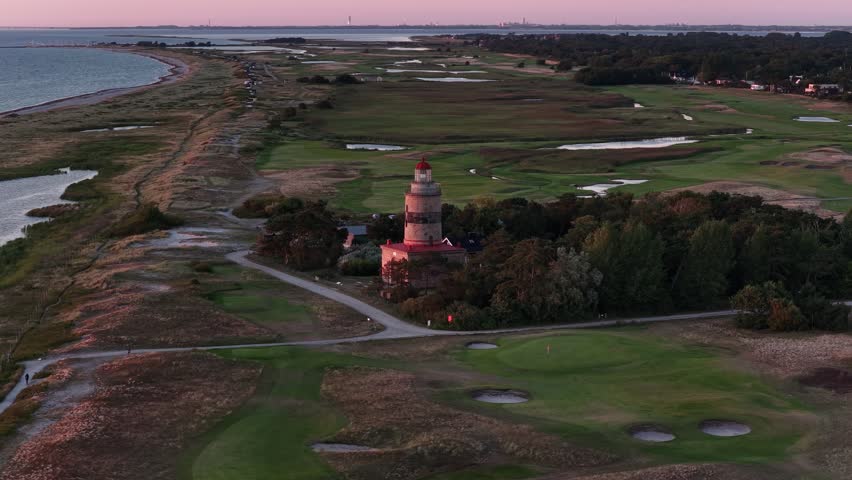 An aerial footage of Falsterbo Lighthouse, surrounded by woods, dunes, and marshes at dusk, with the Baltic Sea beyond in Falsterbo, Sweden