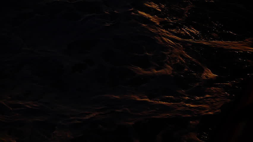 Golden hour ocean surface shimmering with gentle waves and rippling textures, dark water illuminated by warm sunset light, abstract patterns of motion and reflective highlights
