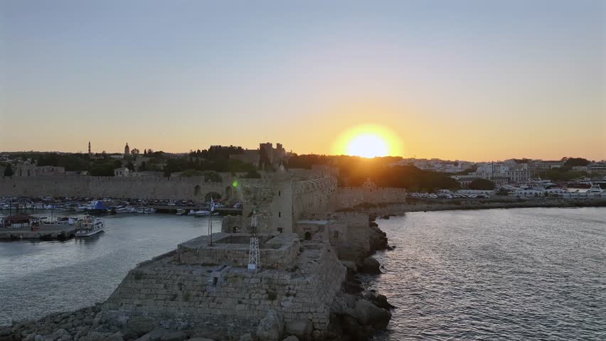 Rhodes, Greece, Mandraki Harbour, historic port with medieval windmills, yachts, and the St. Nicholas Fortress, blending cultural heritage with a lively Mediterranean setting.
