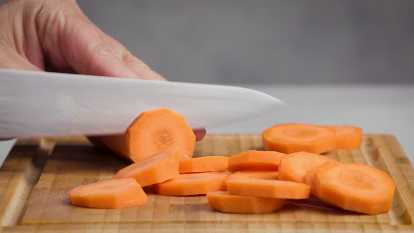 chef cut carrot on cutting board with sharp knife for making healthy meal and cooking, cook cutting carrots for making salad, food closeup in kitchen