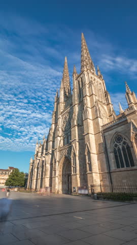 Cathedrale Saint-Andre de Bordeaux timelapse hyperlapse with twin spires under a vibrant blue cloudy sky. People walking in the square create a serene urban atmosphere before sunset. Bordeaux, France