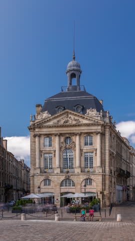Place de la Bourse timelapse hyperlapse in Bordeaux, France, with restaurants surrounded by classic architecture under a cloudy blue sky. People walking around the main square and central streets
