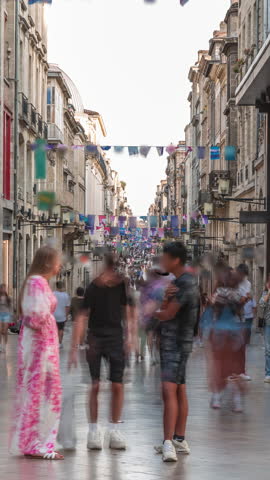 Tourists and locals walking and shopping in Rue Sainte-Catherine timelapse, Bordeaux, France. The longest pedestrian street in the country. Colorful flags decorate the street. Atmosphere of urban life