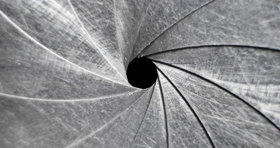 Circular blades of a mechanical iris create a precision opening controlling amount of light entering a camera lens with the opening mechanism controlling the aperture and the depth of field in focus.