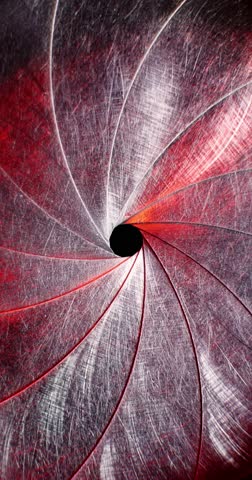 Circular blades of a mechanical iris create a precision opening controlling amount of light entering a camera lens with the opening mechanism controlling the aperture and the depth of field in focus.