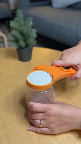 Vertical close-up of hands using an orange jar opener tool to open a kitchen container. Perfect for product ads, DIY tutorials, lifestyle tips, and e-commerce demos.