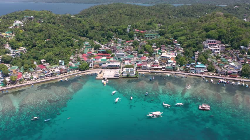 Stunning aerial video captures Puerto Galera and Sabang Bay with turquoise waters, boats, and diving schools, showcasing the tropical beauty of this famous Philippine destination.