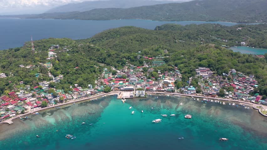 Aerial of Puerto Galera and Sabang Bay with turquoise waters, boats, and diving schools, showcasing the tropical beauty of this famous Philippine destination.