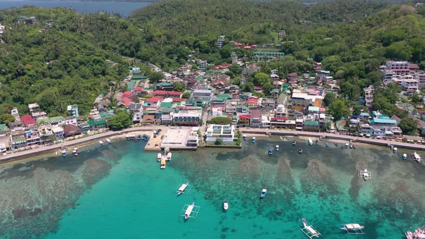 A stunning aerial captures Puerto Galera and Sabang Bay with turquoise waters, boats, and diving schools, showcasing the tropical beauty of this famous Philippine destination.