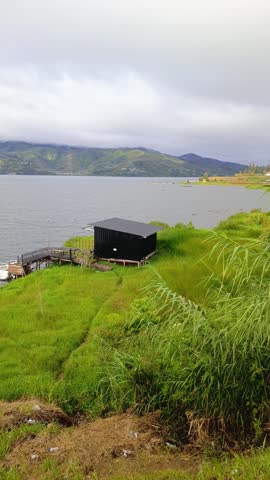 Scenic lake view with green hills and cloudy sky, calm water landscape surrounded by trees and mountains, peaceful nature travel destination and outdoor adventure background
