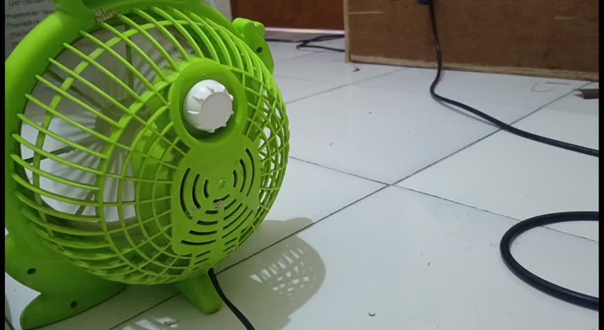 Cute green cartoon-style electric fan shaped like a frog, portable desk fan for home cooling and decoration, small household appliance isolated indoor scene.