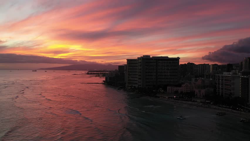 Sunset skyline over Da Nang coast with high-rise buildings silhouetted against the golden sky. Calm ocean waters and distant mountains frame the serene urban-meets-nature seascape.