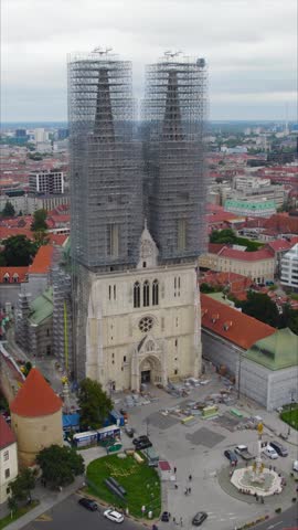 Vertical aerial circling the Majestic Zagreb Cathedral’s front façade under renovation, blending Gothic splendour with the surrounding vibrant cityscape of Croatia’s capital.