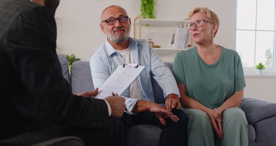 Advisor meets a couple of seniors at home for a finance consultation and contract signing, reviewing each document. Elderly retiered family review and sign contract with real estate agent.