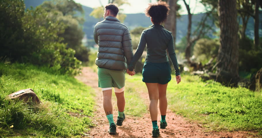 Couple, back and holding hands with hiking trail for sightseeing or outdoor adventure in nature. Man, woman or trekking with path in forest for exercise, commitment or journey together in woods