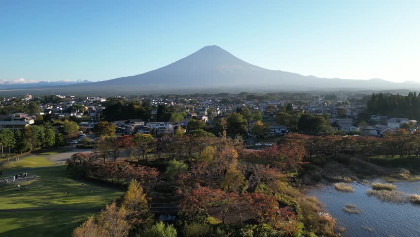 Mount Fuji aerial drone view over Lake Kawaguchi with autumn foliage, vibrant fall colors, Hakone cityscape and clear blue sky on a sunny day, Japan travel landscape scenery.
