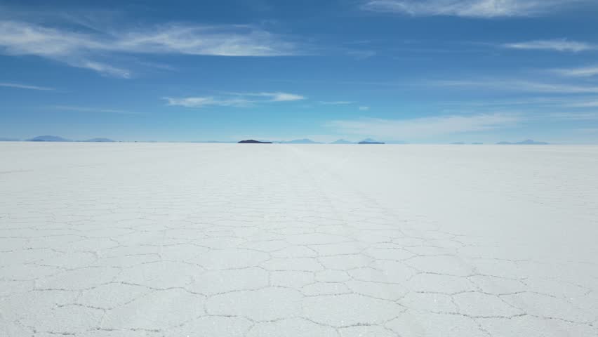 Aerial drone view of Bolivia Uyuni Salt Flats, endless white landscape under clear blue sky, cars driving across reflective surface, stunning natural wonder travel destination.