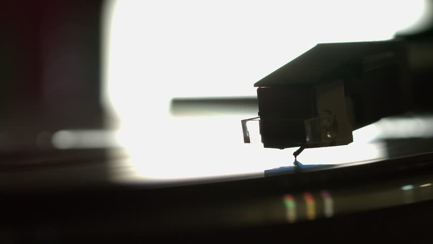 Backlit silhouette of record player needle in album groove, close up