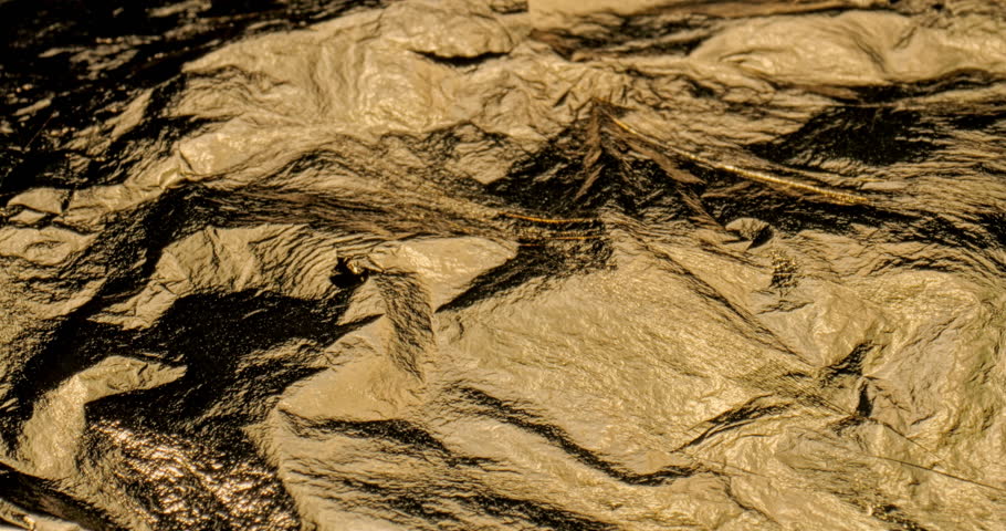 Linear Glide Over Crumpled Gold Foil Surface. Steady horizontal pan across wrinkled metallic gold material.