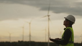 Engineer in safety gear using laptop to monitor wind turbines at renewable energy farm. Concept of clean power, sustainable technology, and smart grid operation. - Powered by Shutterstock - Get 15% off with code: PIKWIZARD15