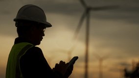 Silhouette of engineer using smartphone to monitor wind turbines at sunset. Concept of remote control, clean energy, smart grid, and renewable power infrastructure. - Powered by Shutterstock - Get 15% off with code: PIKWIZARD15