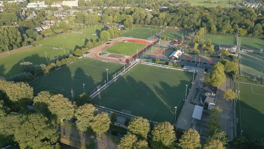 Drone footage showing football fields, athletics track, and sports facilities surrounded by trees.