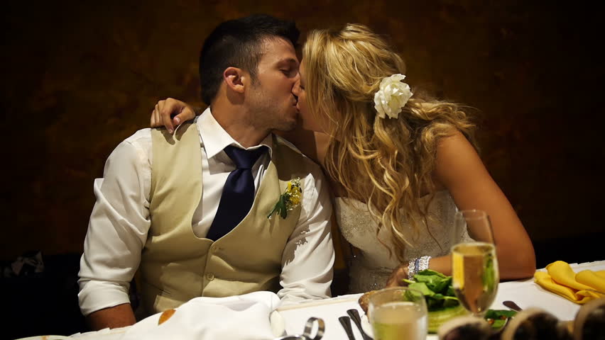 A young couple share a kiss at their wedding reception.