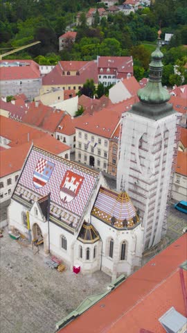 Vertical aerial of St. Mark’s Church in Zagreb, Croatia, highlighting its vibrant tiled roof and two distinctive roof emblems.