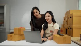 Two young asian women, likely online retailers, celebrate their achievements amidst cardboard boxes in their office - Powered by Shutterstock - Get 15% off with code: PIKWIZARD15
